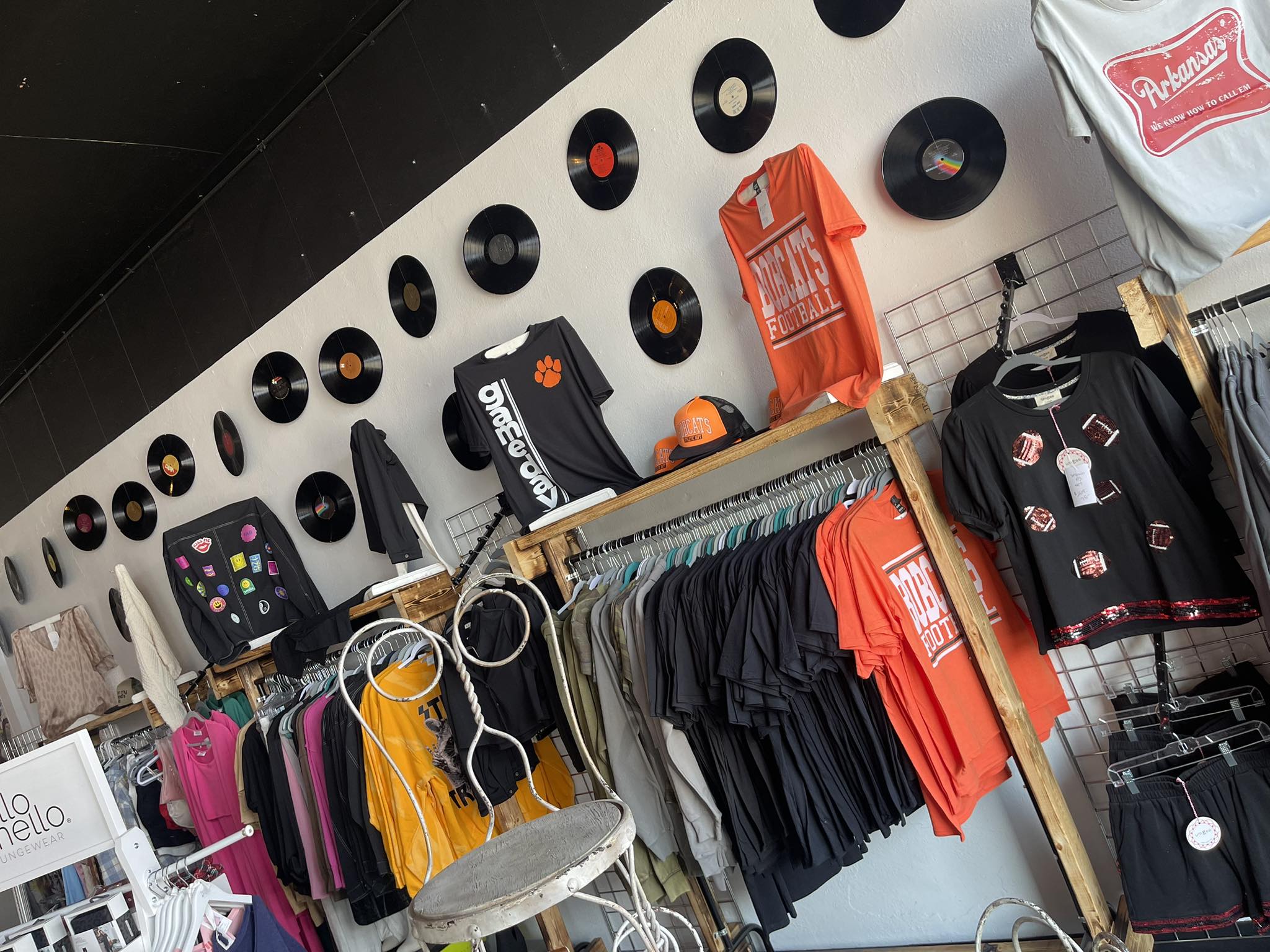 Display of t-shirts and accessories on a wall with vinyl records and a chair.