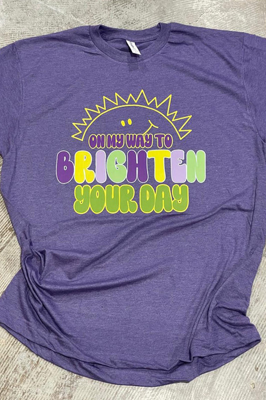 A heather purple t-shirt with the text 'On My Way To Brighten Your Day' and a graphic of a sun with rays on it.