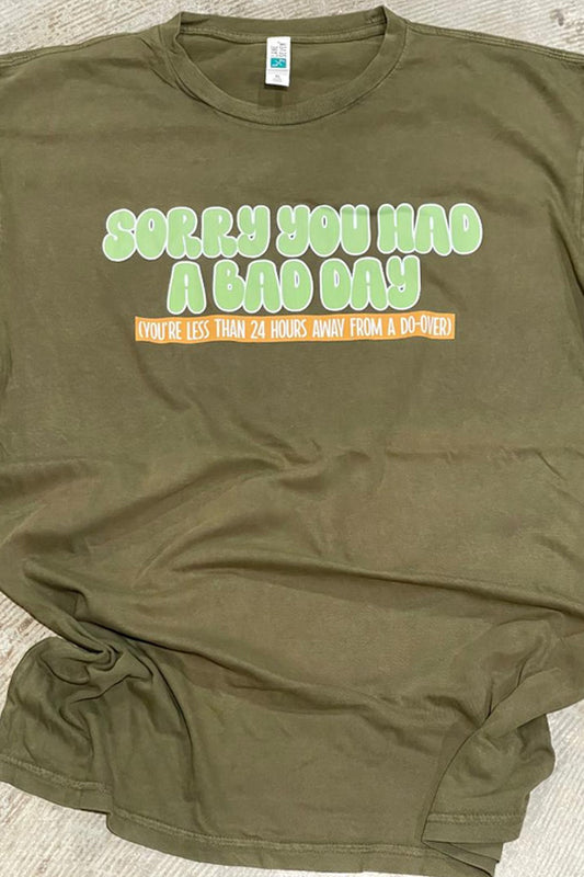 A vintage olive green t-shirt with the text 'Sorry you had a bad day' printed on the front.